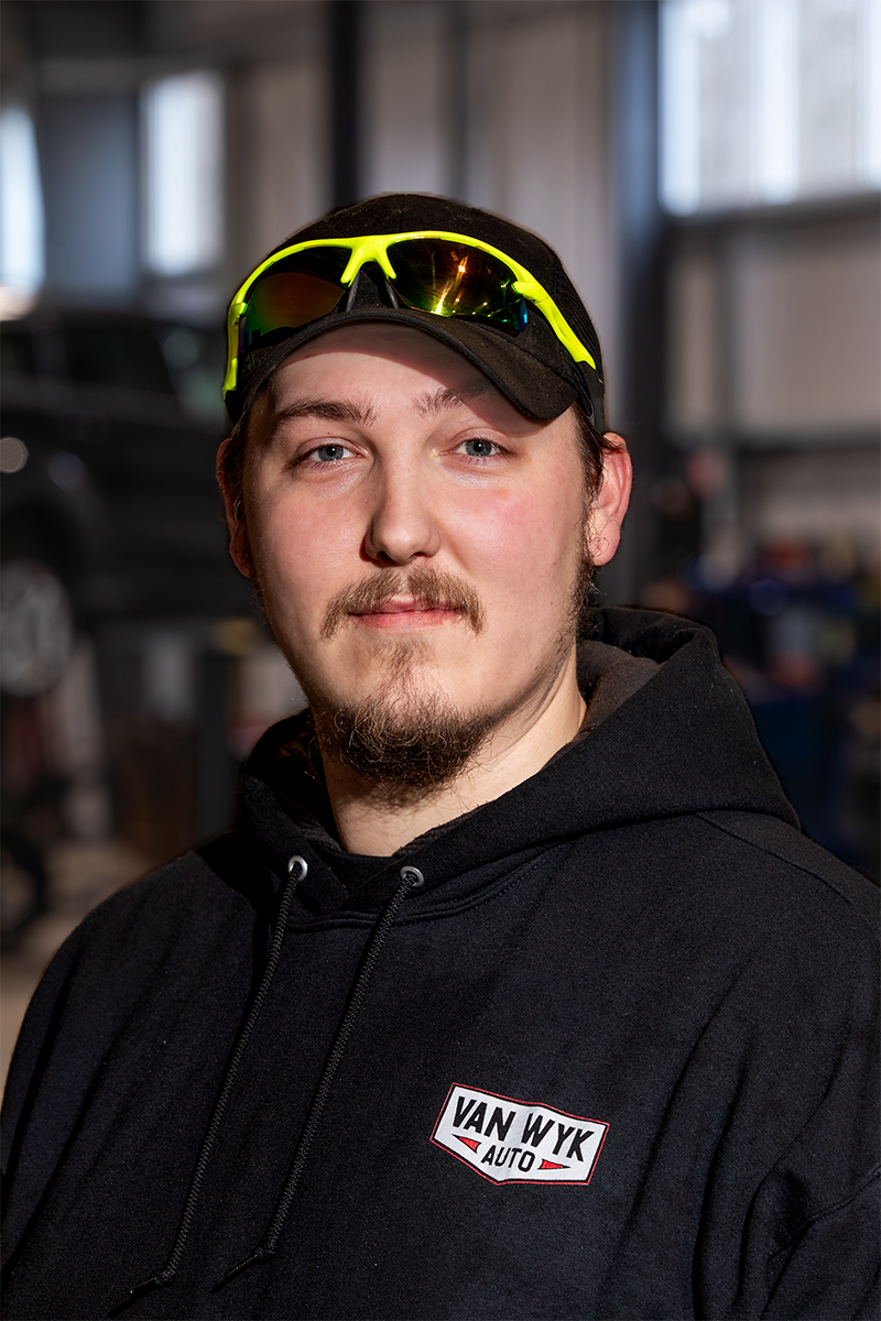 Headshot of Bo, an automotive technician at Van Wyk Auto, smiling in the repair shop.